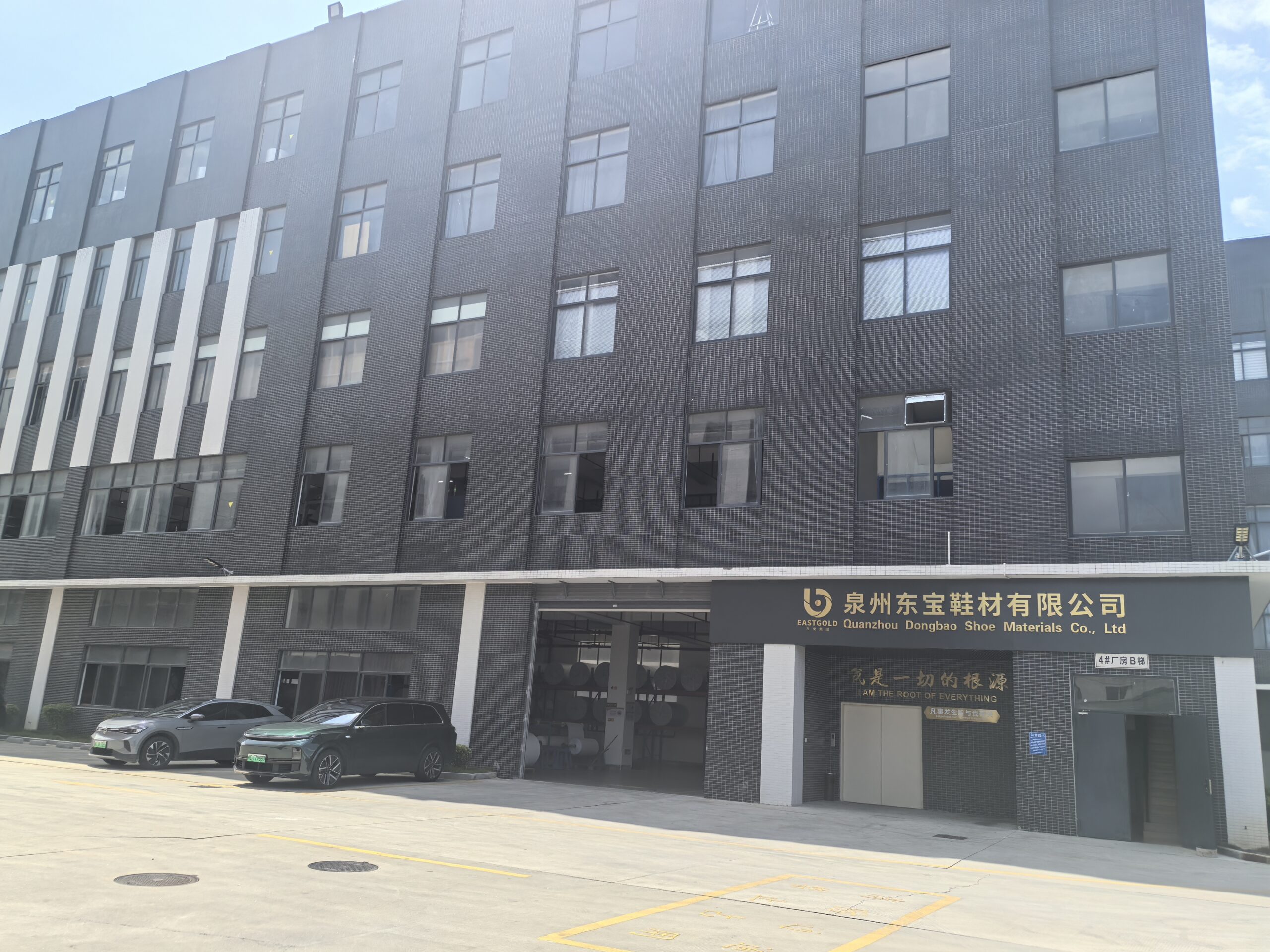 Front view of Quanzhou Dongbao Shoe Materials Co., Ltd. (EASTGOLD): a multi-story light-gray industrial building with a blue exterior stairwell marked